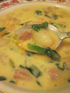 a spoon full of soup sitting on top of a white and yellow plate with green vegetables