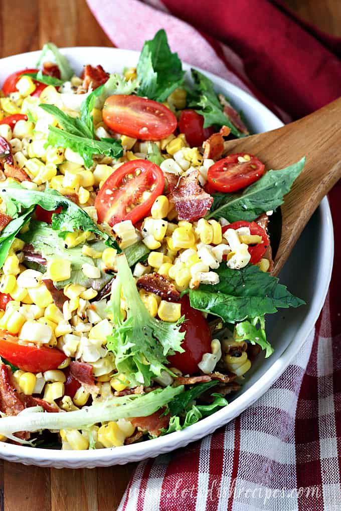 a salad with corn, tomatoes and lettuce in a white bowl on a wooden table