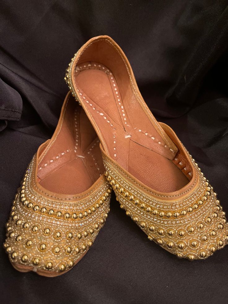 A beautiful masterpiece handcrafted from the heartland of Punjab (India) in gold with beads, zari and katdana. A sure piece to add on to your collection, will go with most of your outfits. Extra cushion for superior comfort. If you desire another size other tan the one available, we can customize it to your requirements. However, shipping would take a little longer. We can also customize mommy and baby/ kids matching Jutti/ Mojari. All you need is to provide us with the measurements of the foot from heel to big toe. Kundan Traditional Wear With Gold Embroidery, Gold Traditional Wear With Gota Work For Wedding, Gold Traditional Wear For Wedding And Navratri, Gold Traditional Wear For Wedding Festivities, Traditional Wedding Wear With Gold Embroidery, Festive Gold Traditional Wear For Wedding, Gold Traditional Wear For Wedding And Festive Occasions, Gold Traditional Wedding Wear For Festive Occasions, Traditional Wear With Gold Embroidery For Diwali