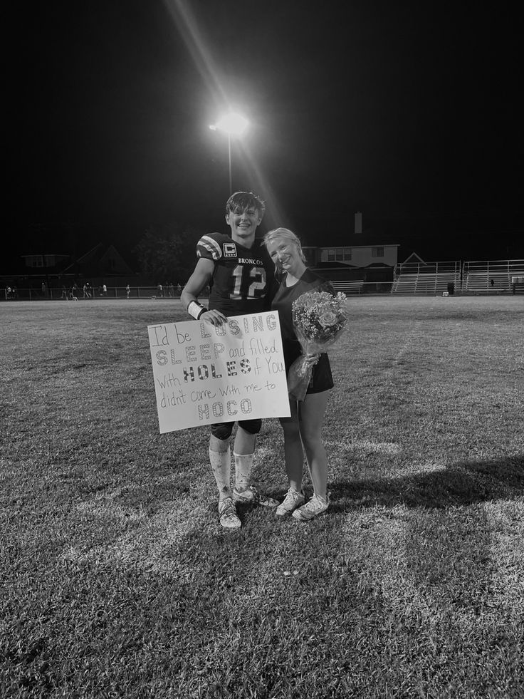 two people standing on top of a field holding a sign