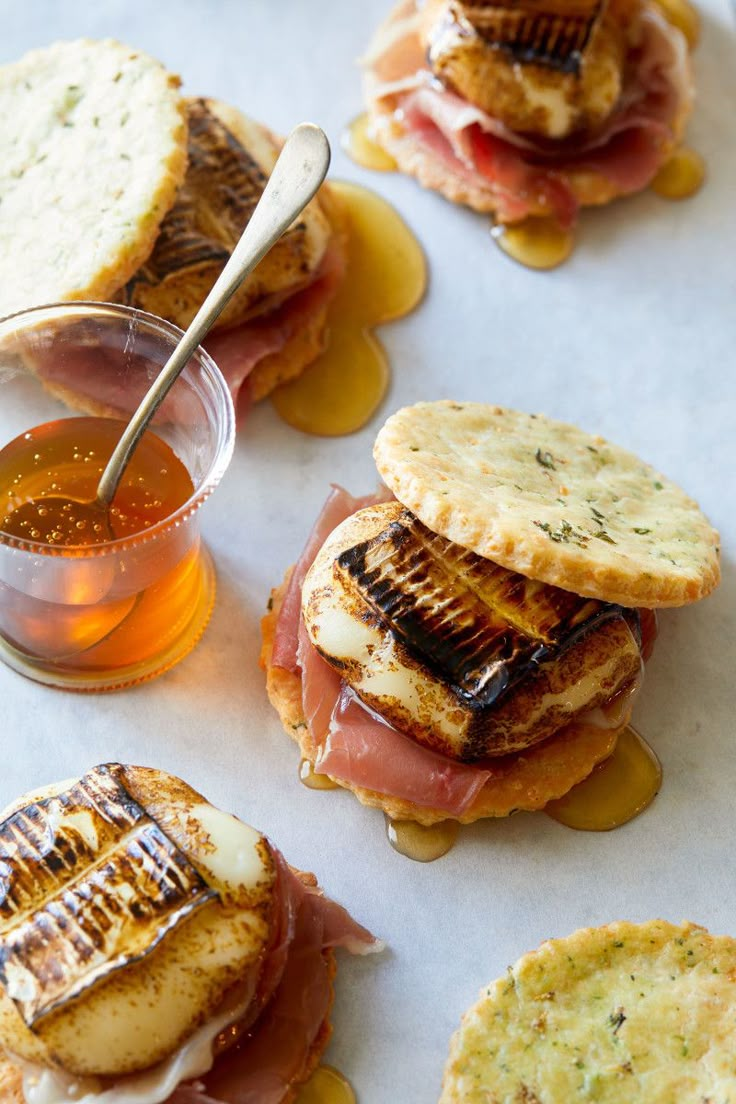 small sandwiches with meat and cheese on them next to a cup of tea or honey