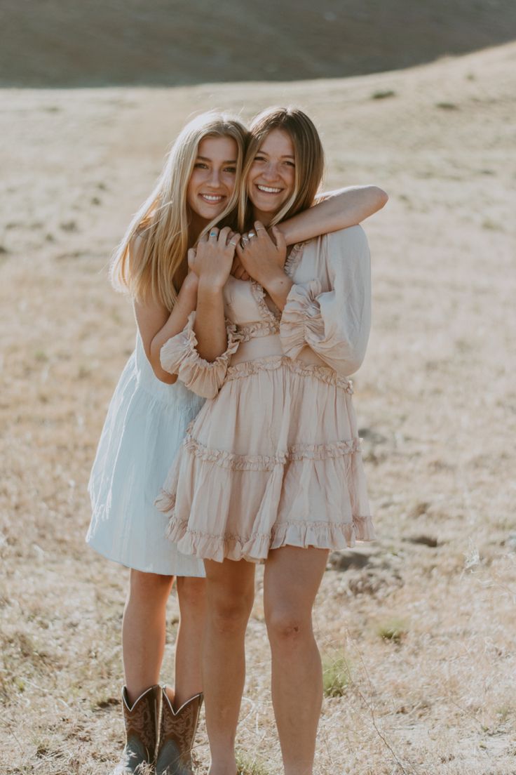 two young women standing next to each other on top of a dry grass covered field