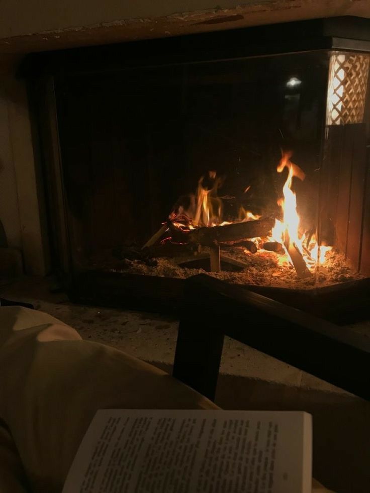 an open book is sitting in front of a fireplace with fire and flames burning inside