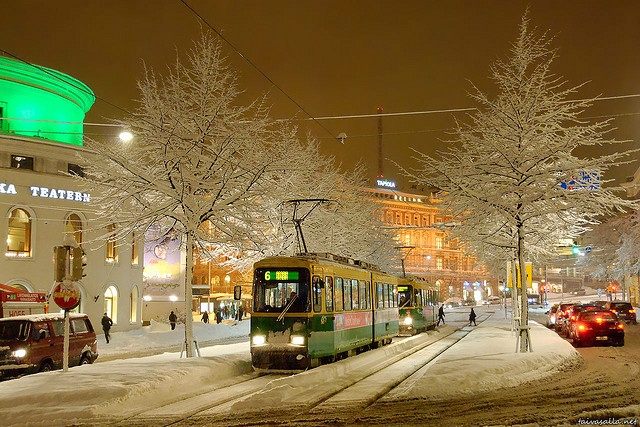 a trolley is driving down the snowy street in front of some buildings and trees with snow on them