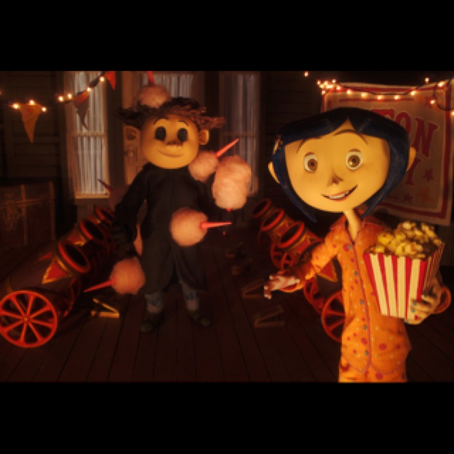 two people standing next to each other in front of an animated movie character and popcorn cart