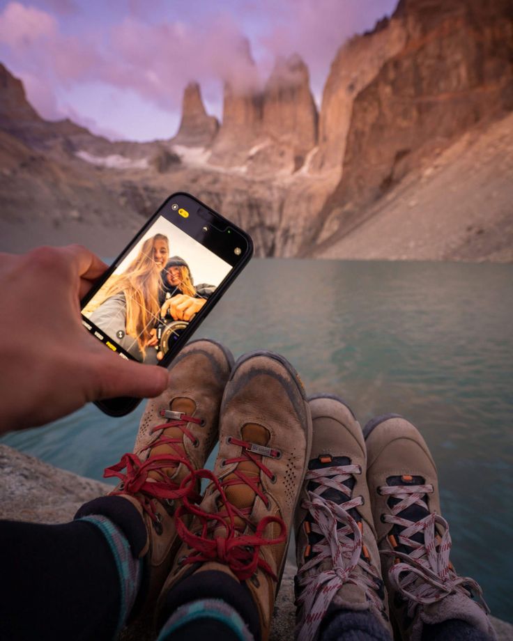 someone taking a photo with their cell phone in front of some mountains and water at sunset