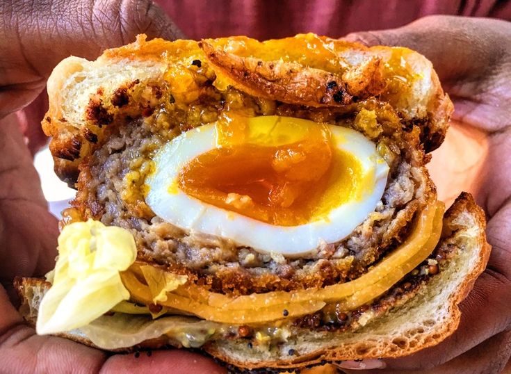 a person holding a sandwich with an egg in the middle and mustard on top,