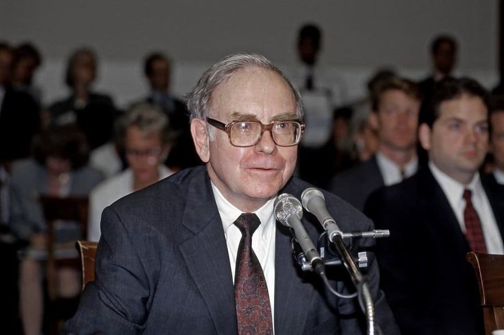 a man sitting at a table in front of a microphone with other people behind him