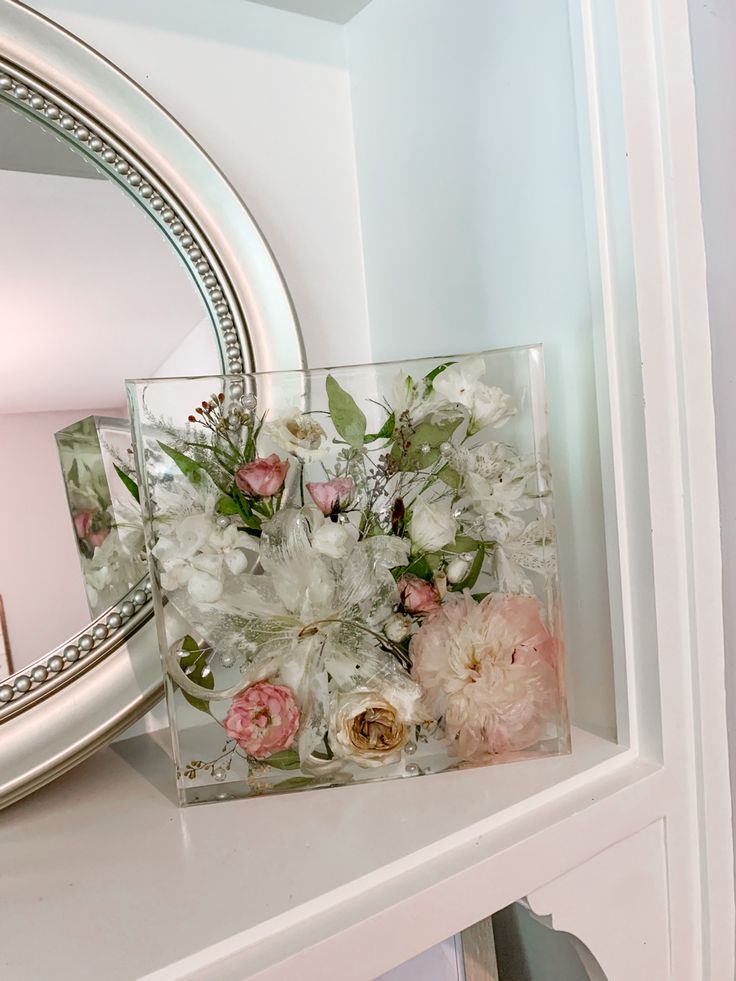 a vase with flowers in it sitting on a shelf next to a mirror and lamp