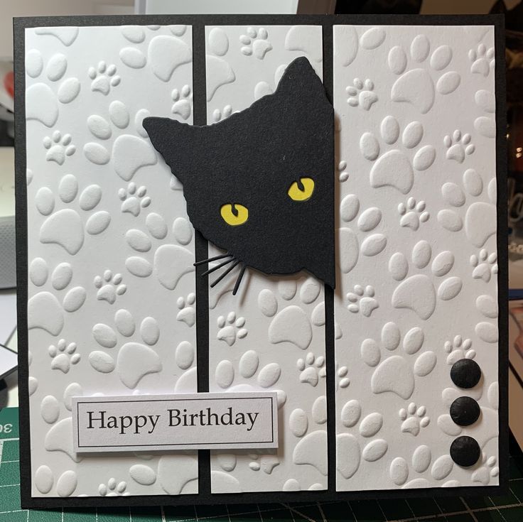 a black cat with yellow eyes is sitting on a card that says, happy birthday