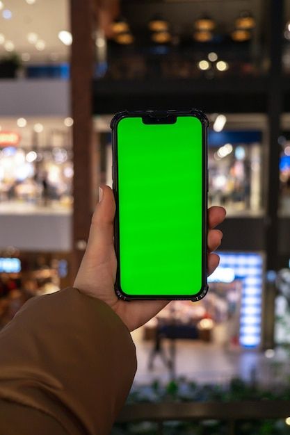 a person holding up a cell phone with a green screen in front of a mall