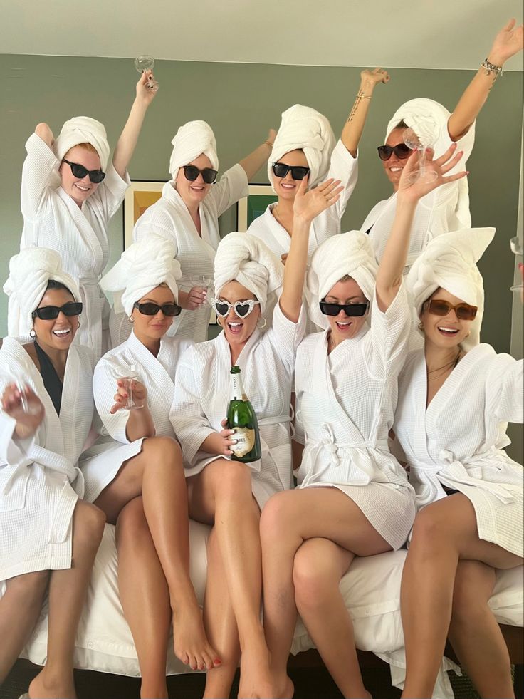 a group of women sitting on top of a bed wearing white robes and holding up their hands