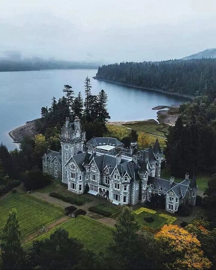 an aerial view of a large house with trees around it and water in the background