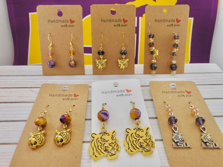 (Beginning with top left to right) 1.  Rain Flower bead with amber crystal with  gold plated ear wires. Total length 24mm, Drop 18mm and the   width is 8mm. 2.  Tiger head charm with purple crystal, on gold plated ear wires. 30mm drop earrings. 3.  Kidney wire Drop earrings, with Purple and gold crystals. Total length 50mm, drop length 20mm, and    the width is 8mm. 4.  Tiger head charm with 10mm metallic purple/gold beads.  35mm drop earrings. 5.   Large Tiger head with Purple/Gold Agate beads. Gold Round Beads Earrings For Gift, Gold Crystal Earrings As Gift, Adjustable Gold Crystal Earrings Nickel Free, Gold Beaded Drop Earrings For Gift, Gold Dangle Crystal Earrings For Gift, Amber Beaded Earrings For Gift, Gold Wire Wrapped Crystal Earrings As Gift, Gold Crystal Earrings With Round Beads On Ear Wire, Gold Crystal Earrings With Lever Back For Gifts