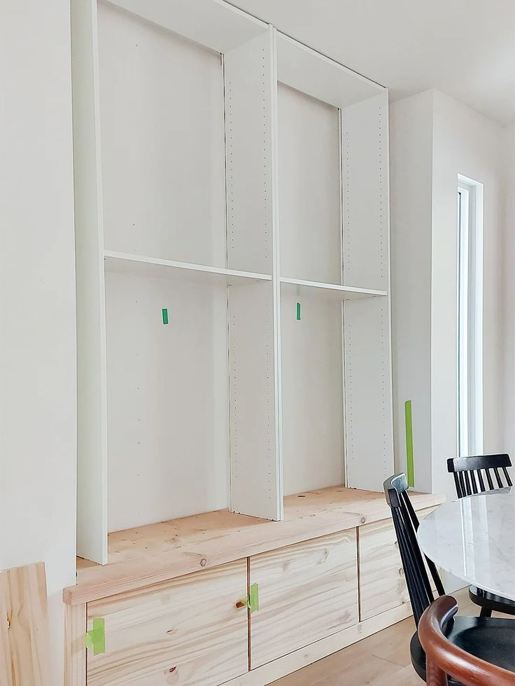 a dining room table and chairs in front of white bookcases with green tags on them