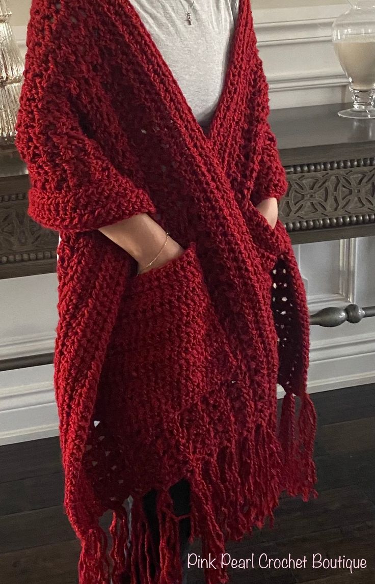 a woman standing in front of a fireplace wearing a red knitted shawl with tassels