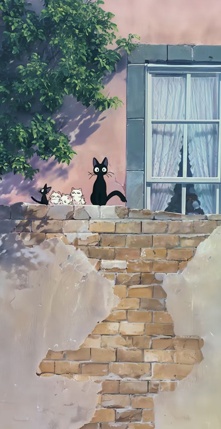 two black cats sitting on top of a brick wall next to a tree and window