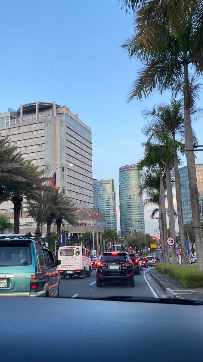 cars driving down the road in front of tall buildings and palm trees on both sides