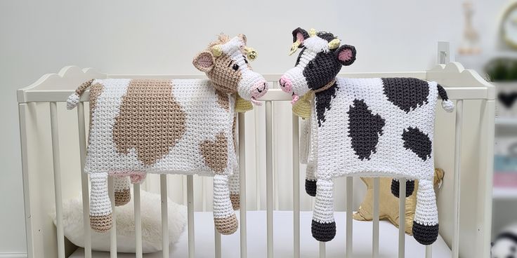 two crocheted stuffed cows standing next to each other in a crib,