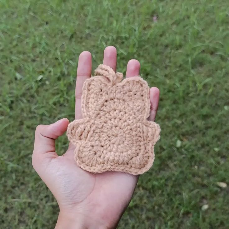 someone is holding up a crocheted object in their hand on the grass outside