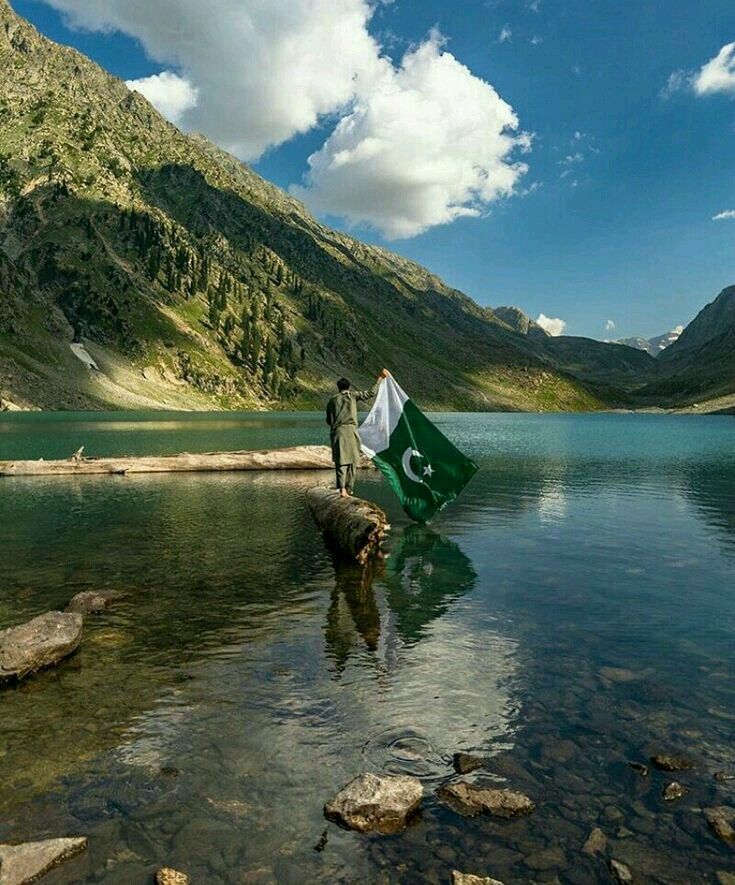 two people holding a flag standing in the middle of a lake with mountains in the background