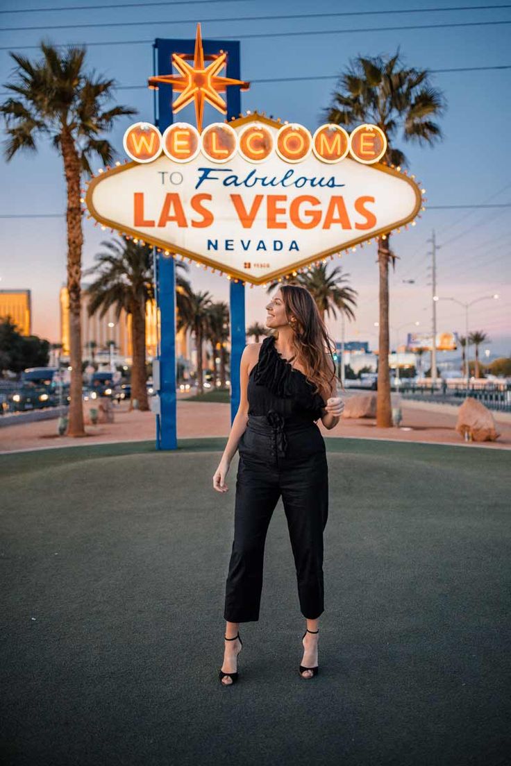 a woman standing in front of the welcome to fabulous las vegas sign