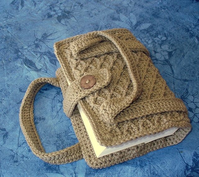 a crocheted book bag sitting on top of a blue cloth covered tablecloth