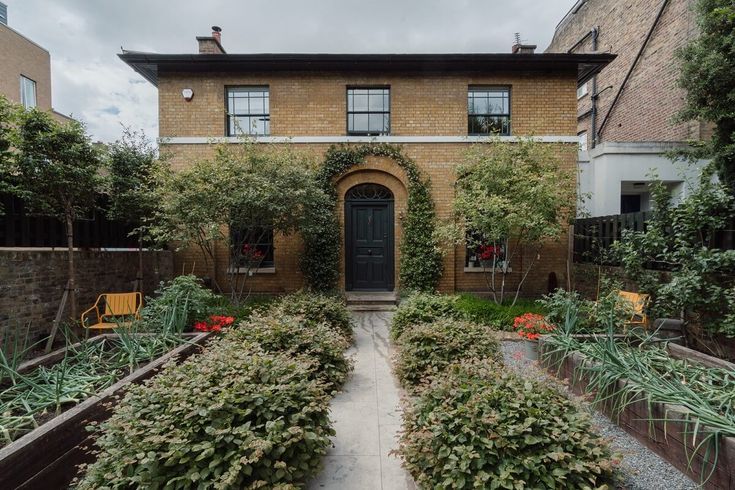 a house with many plants in front of it and a walkway leading to the door