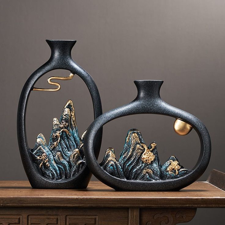 two black vases sitting on top of a wooden table with mountains in the background