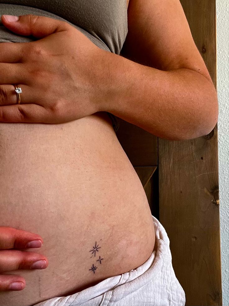 a pregnant woman's belly with her hand on the side and stars tattoo on it