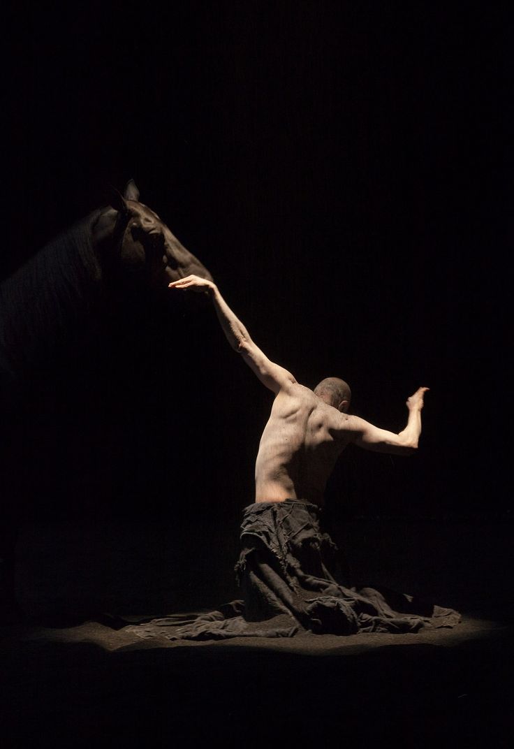 a male ballet dancer in the dark with his arms stretched out and one leg bent forward