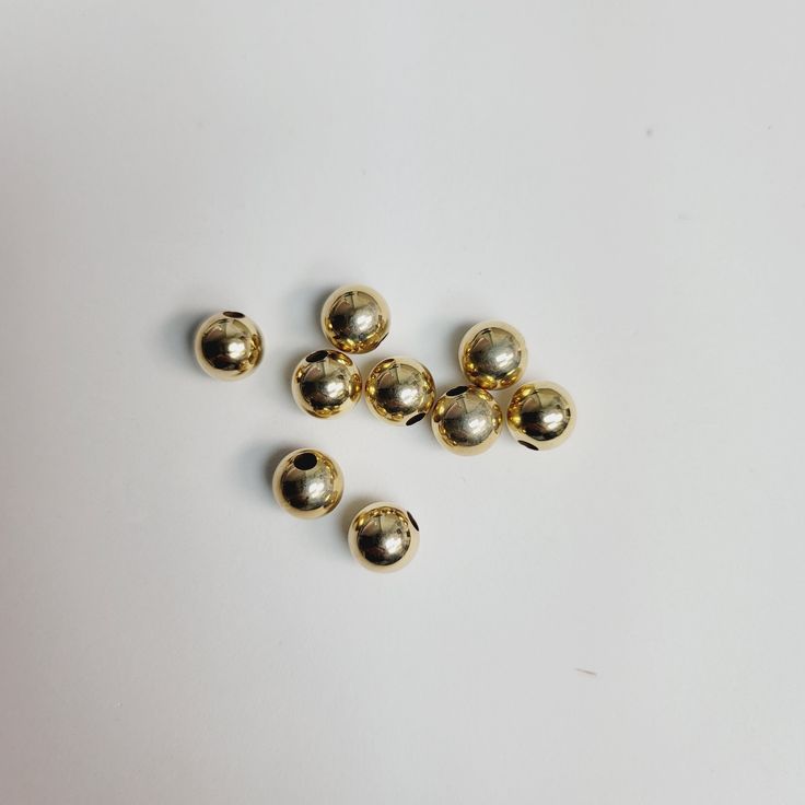 several gold colored beads on a white surface with one bead missing from the middle