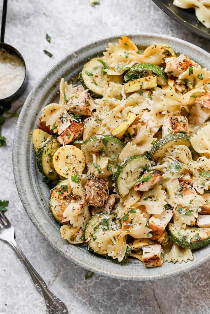 a bowl filled with pasta and vegetables on top of a white table next to silverware