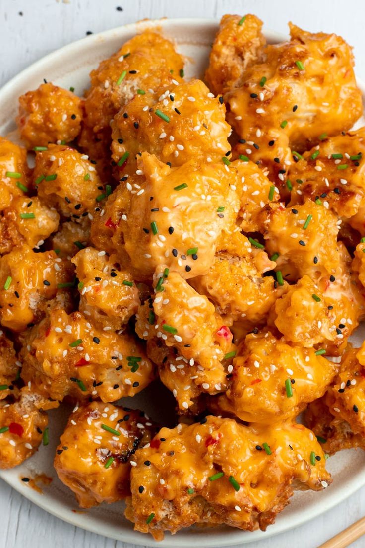 a white plate topped with chicken covered in sesame seeds and seasoning next to chopsticks