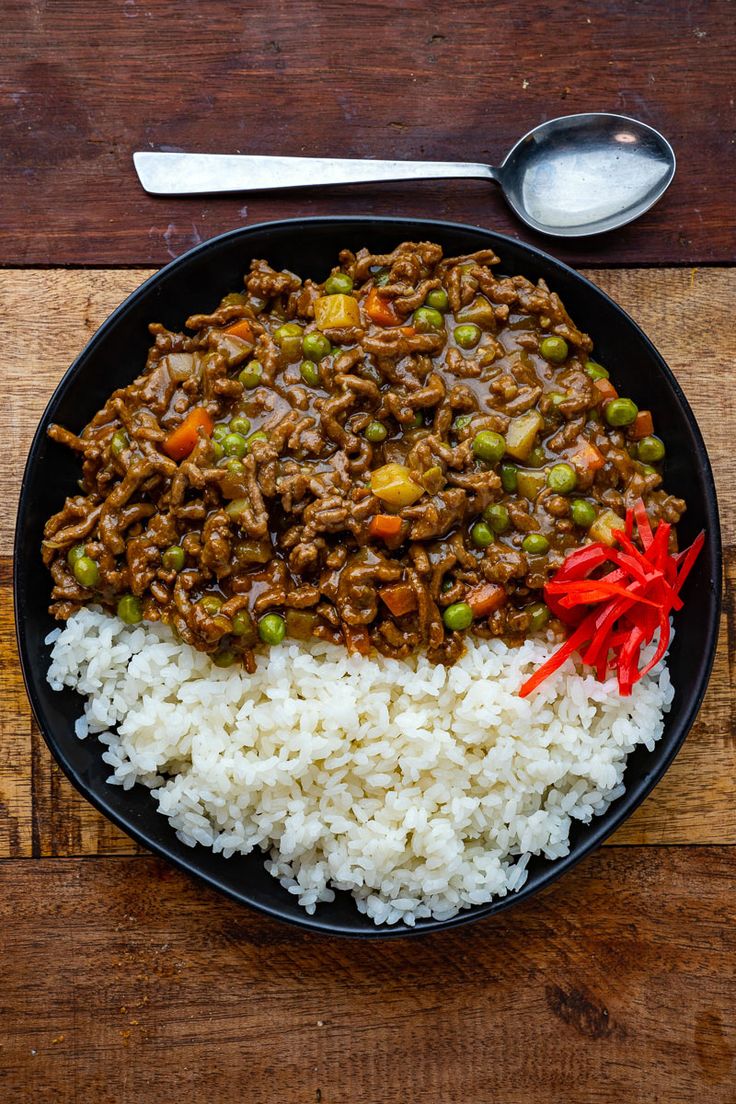 a plate with rice, meat and vegetables on it next to a spoon in the bowl