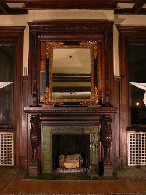 an old fireplace in a room with wooden paneling and white drapes on the windows