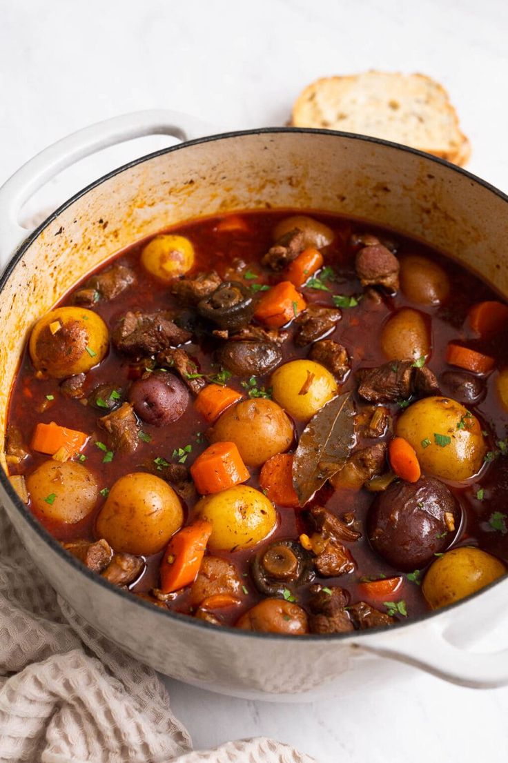 a pot filled with stew next to bread on a white counter top and a napkin