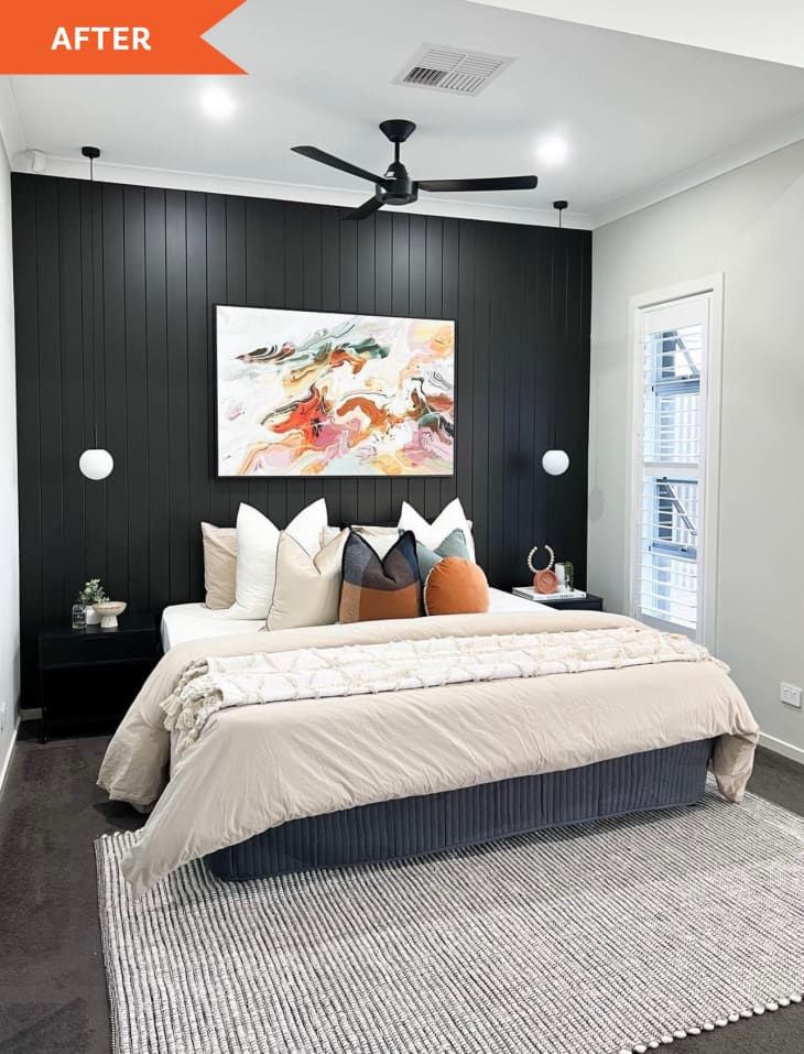 a bedroom with black paneling and white bedding is pictured in this image, it has a ceiling fan that lights up the room