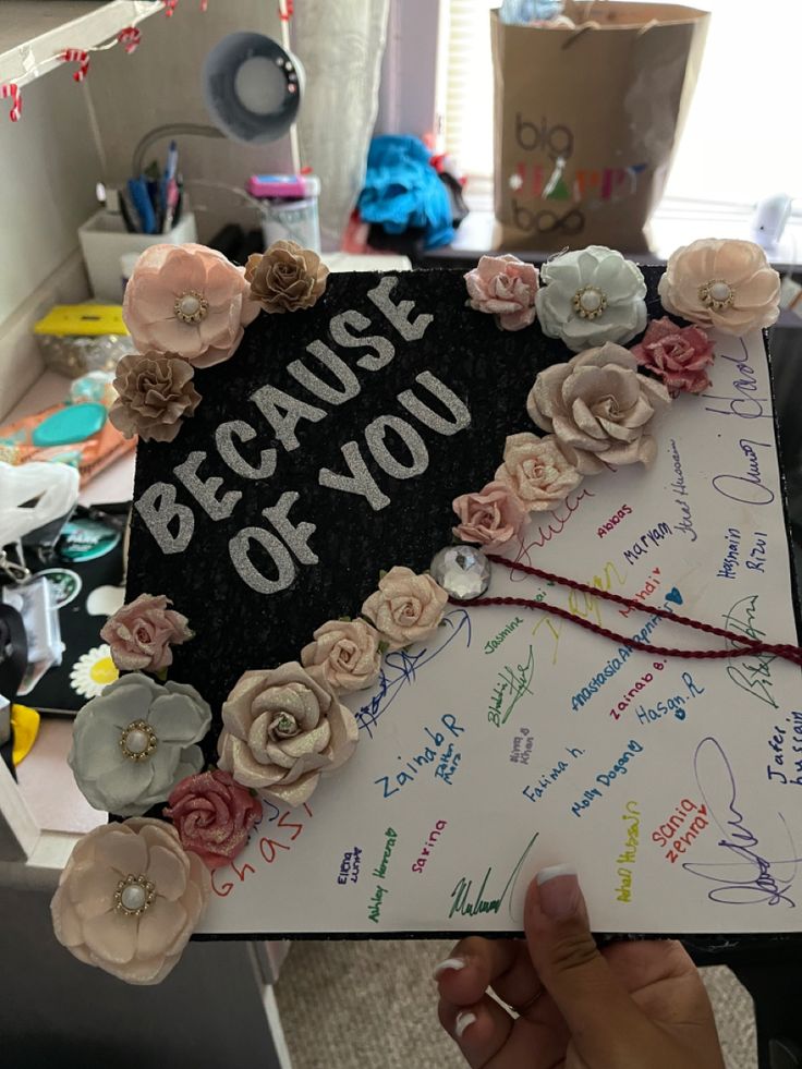 someone is holding up a graduation cap with flowers and writing on it that says because of you