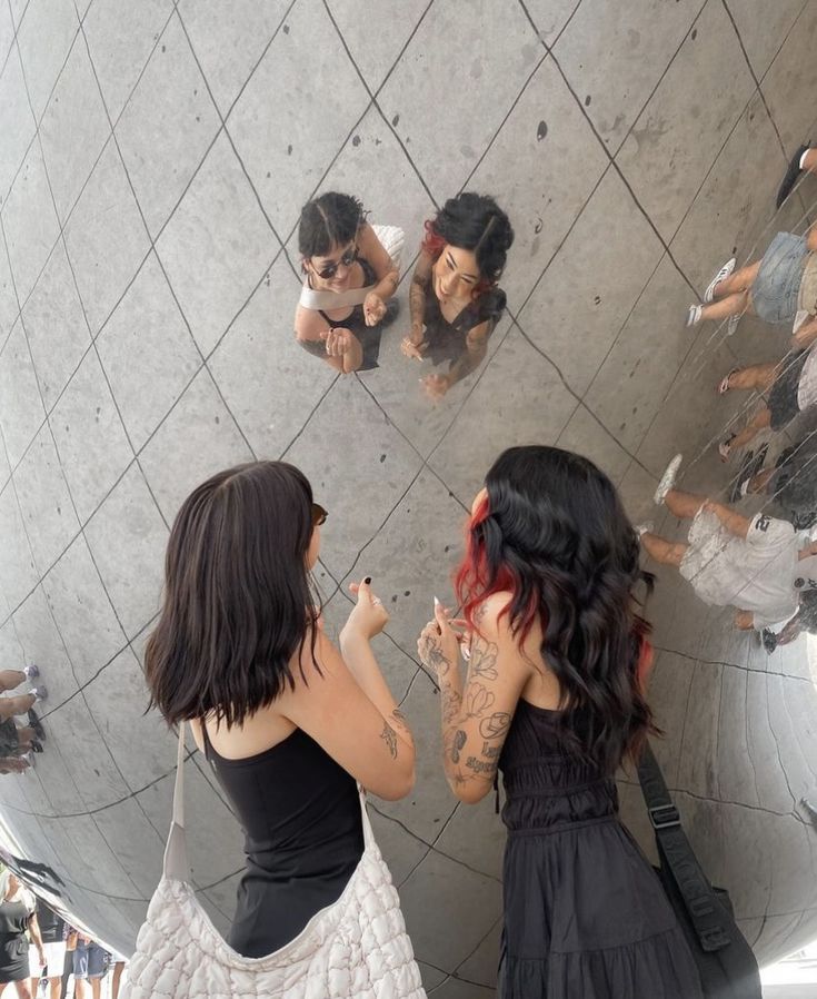 two women standing in front of a mirror with their reflection on the wall behind them