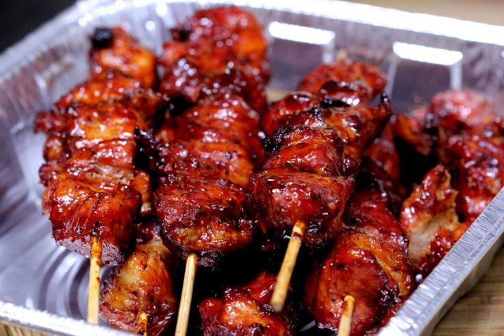 several skewers of chicken on sticks in a tin foil container with ketchup