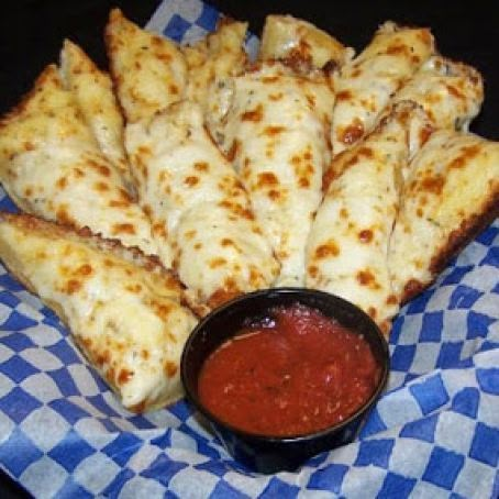 some pizza sticks are on a blue and white checkered paper with a small bowl of sauce