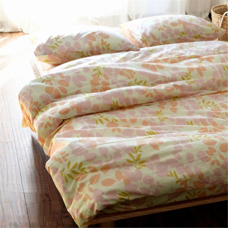 an unmade bed with pink flowers on it in front of a window and wooden floor