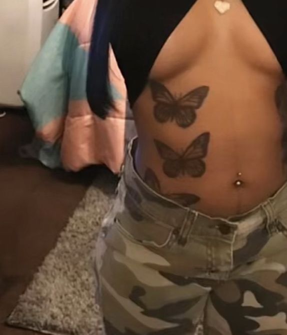 a woman with butterfly tattoos on her stomach and back, standing in front of a bed