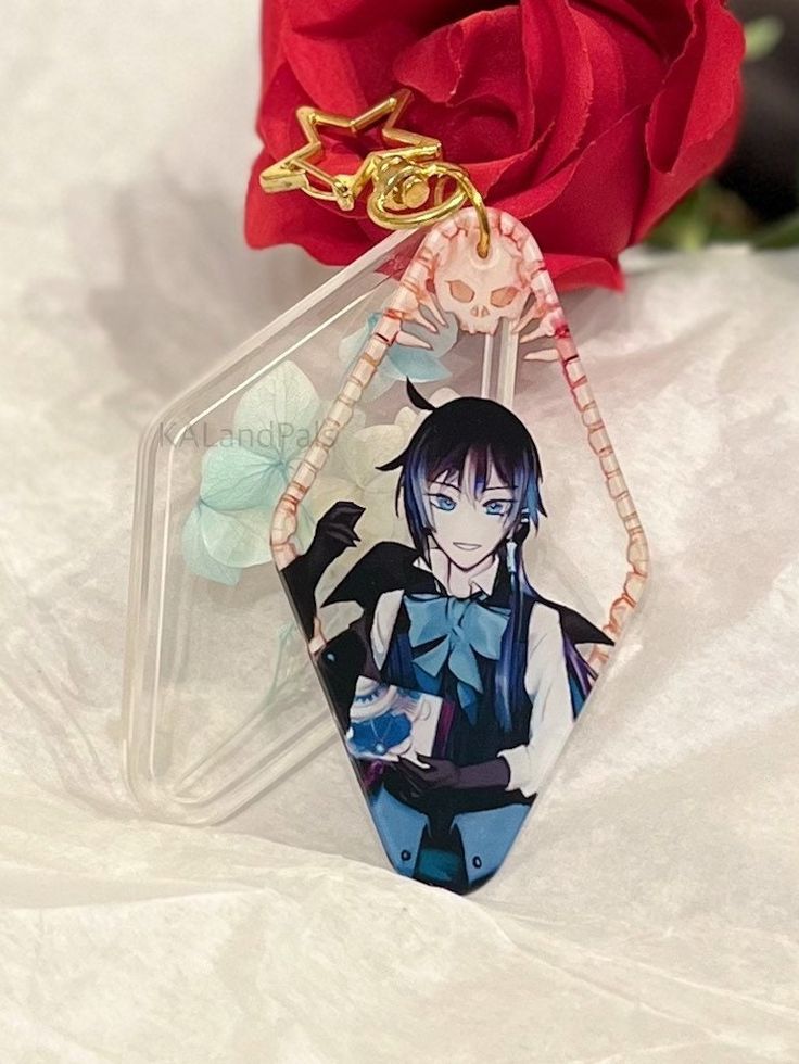 a keychain with an anime character on it sitting next to a red rose