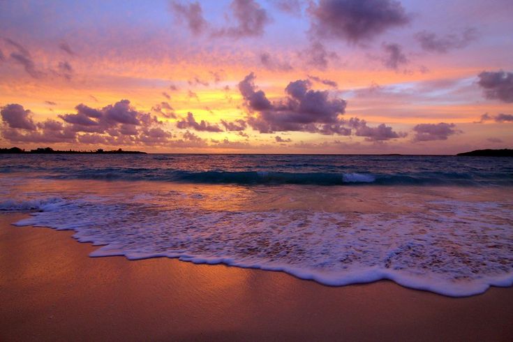 the sun is setting over the ocean with waves coming in to shore and clouds above