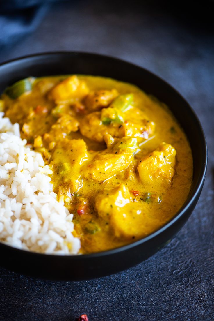 a black bowl filled with rice and chicken curry next to a red pepper shaker