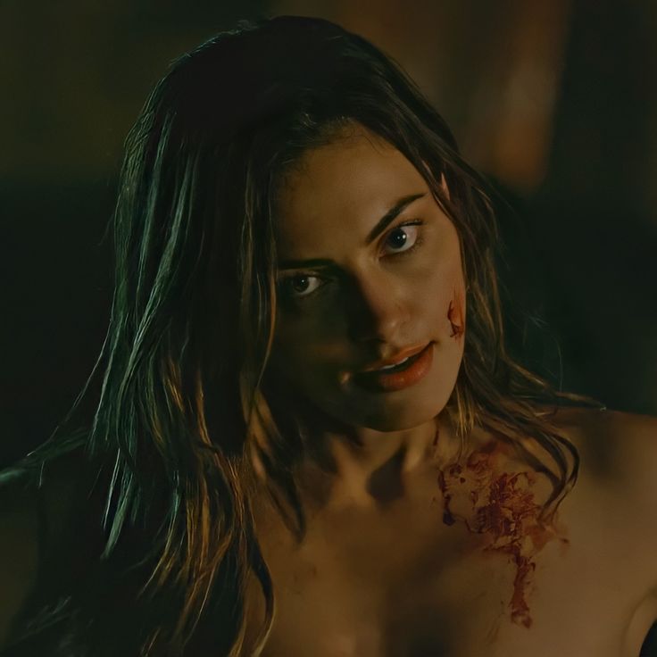 a shirtless woman with blood on her chest and face is looking at the camera