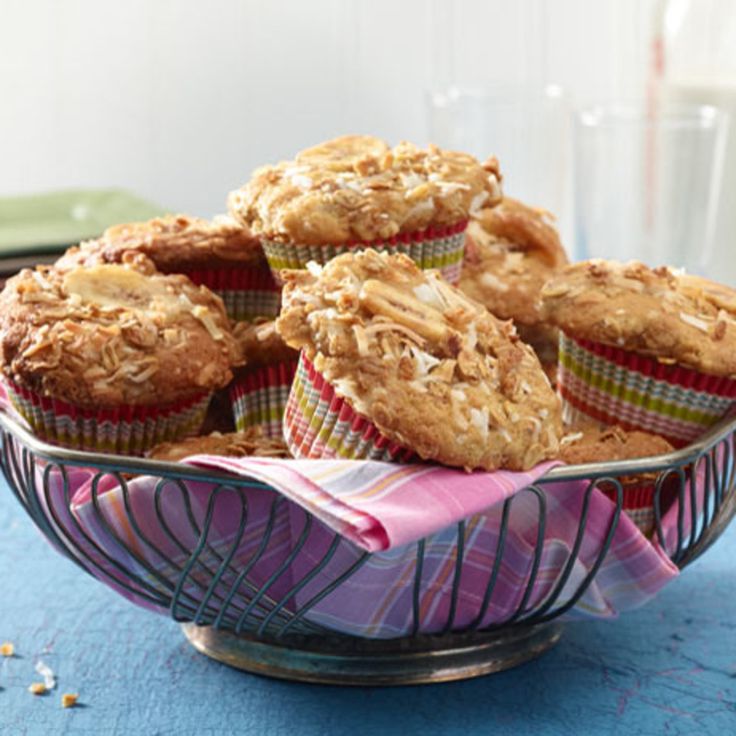 some muffins are sitting in a bowl on a blue tablecloth with a pink napkin