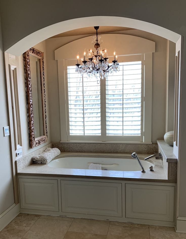 a large bath tub sitting under a window next to a chandelier